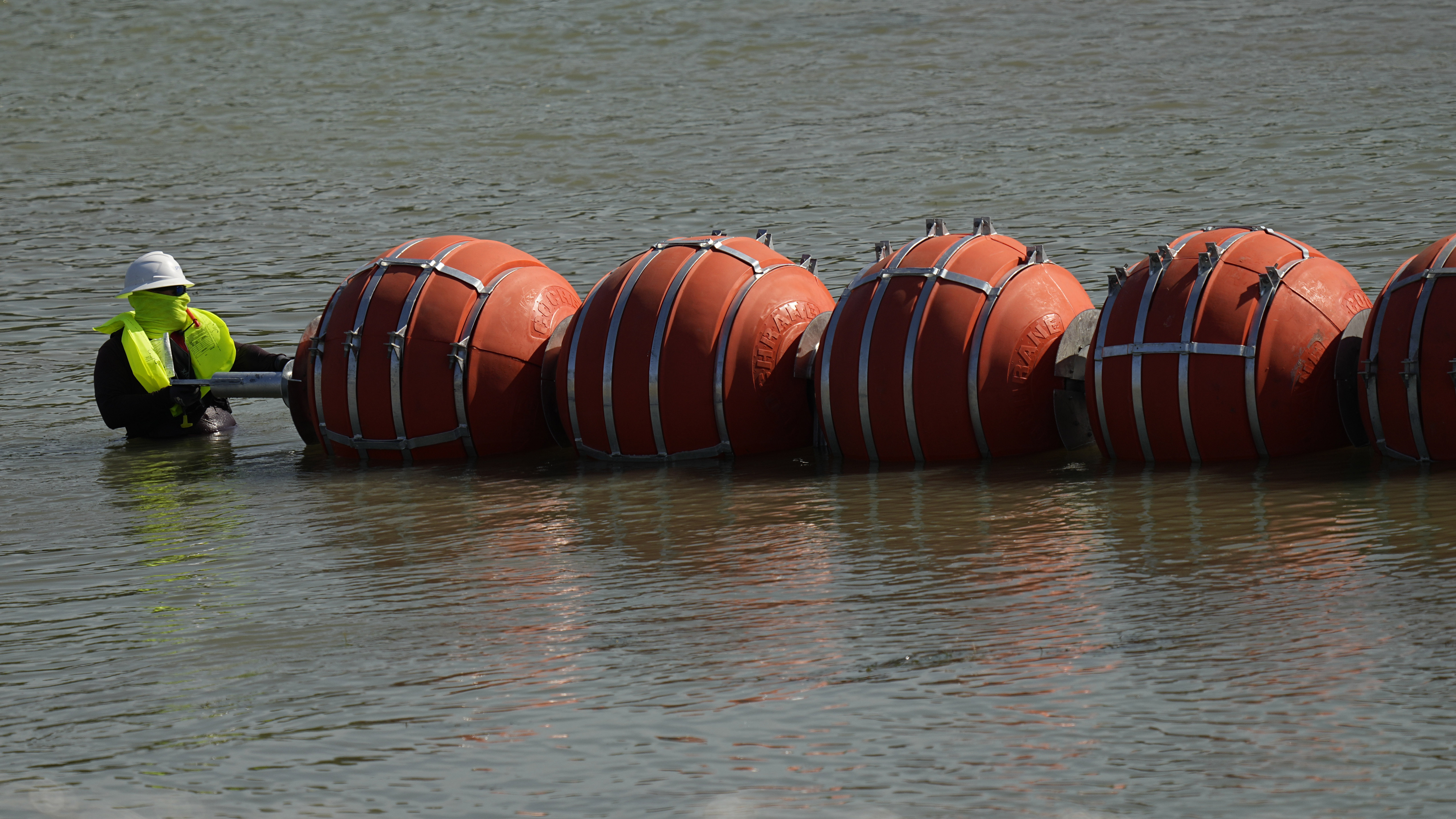 A worker helps deploy a string of large buoys to be used as a border barrier at the center of the Rio Grande near Eagle Pass, Texas, on July 11.