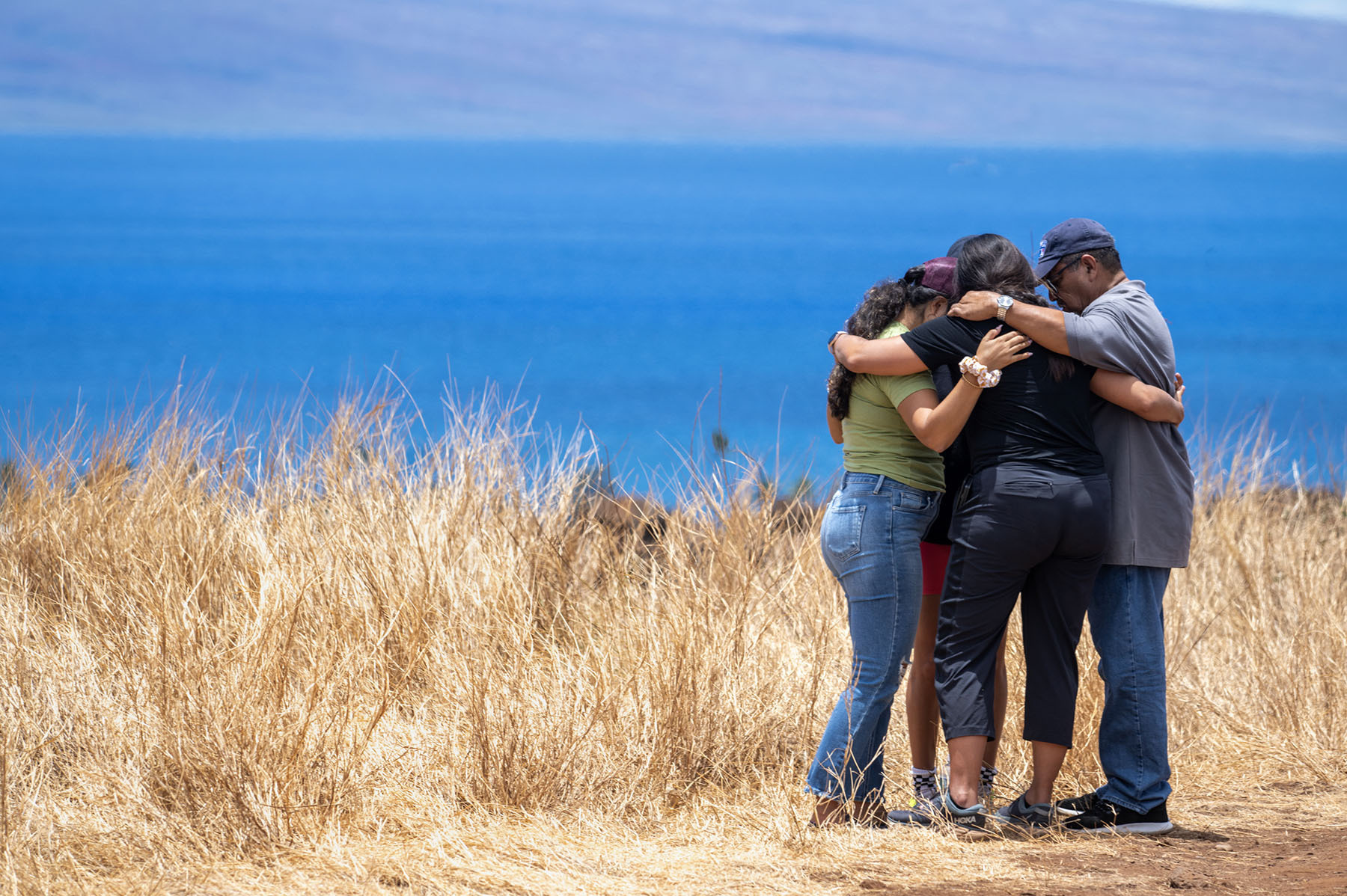 Volunteers helping those who lost homes in Lahaina stop to pray on a hillside. The town is surrounded by dry, invasive grasses which are highly flammable. (Deanne Fitzmaurice for NPR)