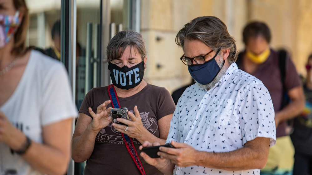 Voters check their phones while waiting to cast in-person ballots at a polling location in Austin, Texas, on Oct. 13, 2020. Many Americans wonder why they can't vote online, on their phones, but experts agree that it's not secure. (Getty Images)