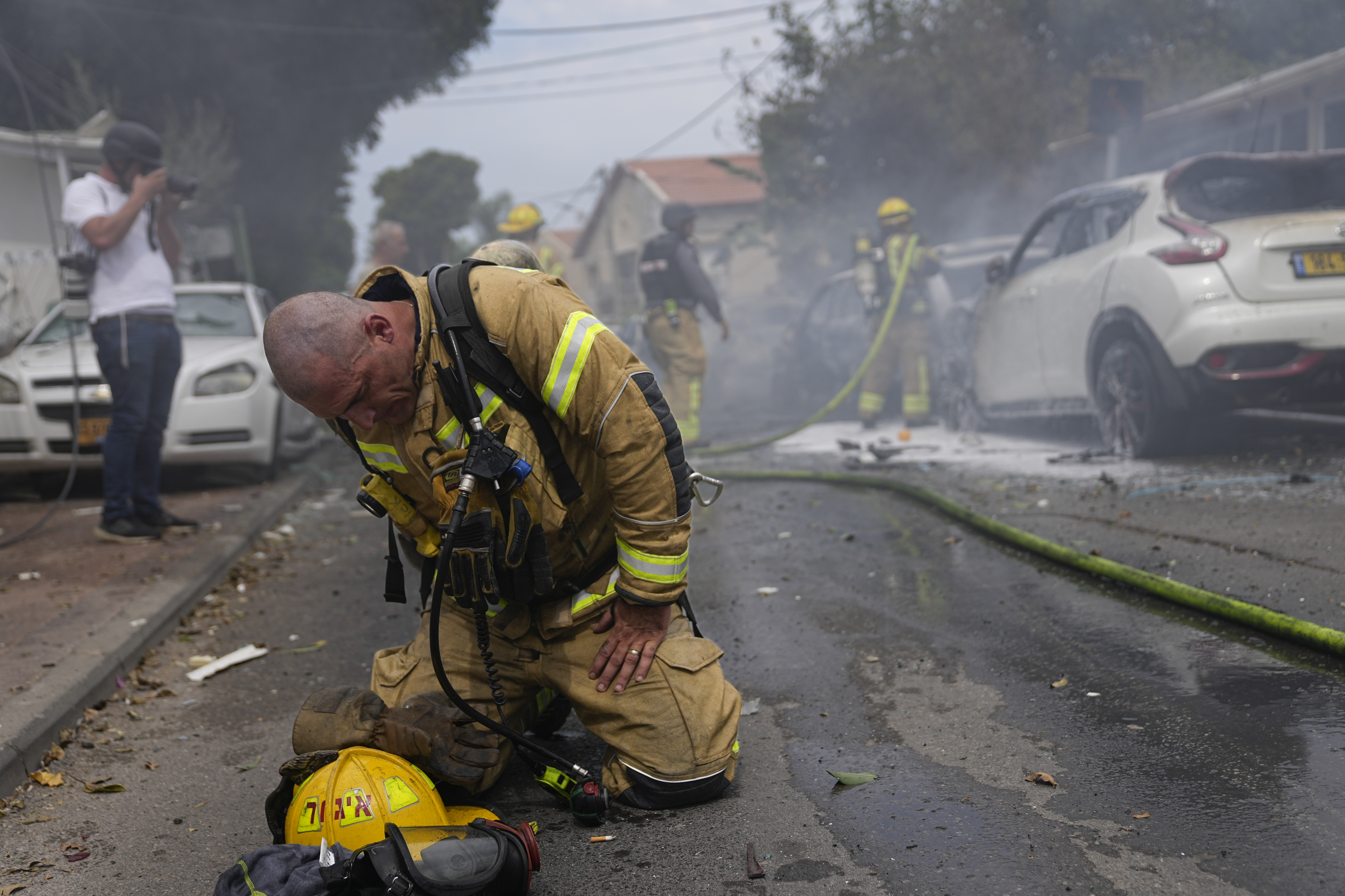 An Israeli firefighter kneels to compose himself after he and his colleagues extinguished cars set on fire by a rocket fired from the Gaza Strip in Ashkelon, Israel, Monday, Oct. 9, 2023.
