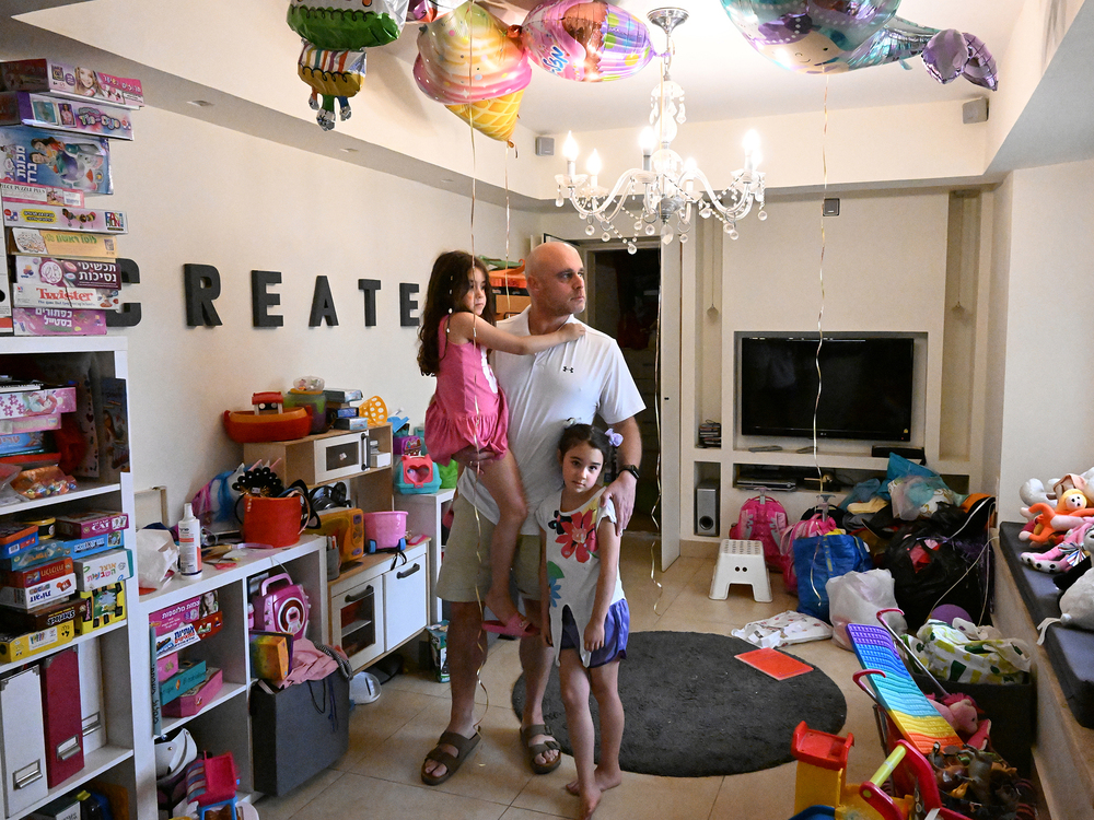 Ido Dan, an uncle to three children feared abducted by Hamas and taken to Gaza, stands for a portrait with his twin daughters. The remnants of their sixth birthday party, which took place the same day as the incursion, are still around the house. (NOOR for NPR)