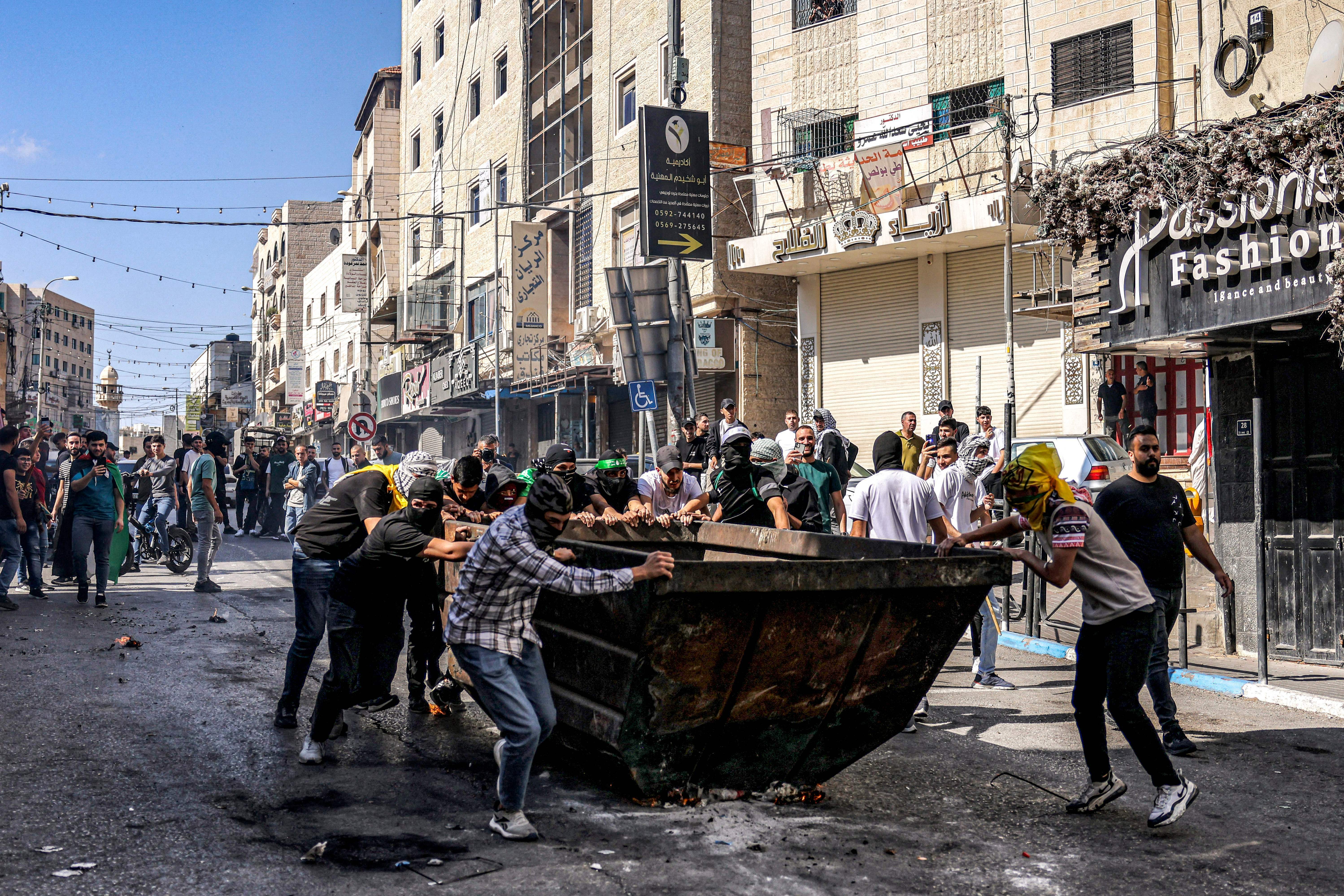 Fri., Oct. 13: Palestinian protesters push a dumpster to be used for cover during clashes with Israeli forces following a rally in solidarity with Gaza by supporters of the Fatah and Hamas movements, in the city of Hebron.