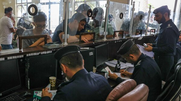 People stand behind a glass barrier as their documents are inspected. They are waiting to leave Gaza and cross over the Rafah border into Egypt. 
