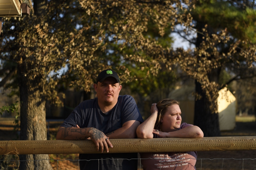 Army veteran Ray Queen stands with his wife, Rebecca Queen, outside their home in Bartlesville, Okla. An NPR investigation has found that thousands of U.S. military service members and veterans, including the Queen family, are at risk of losing their homes through no fault of their own. (Michael Noble Jr. for NPR)