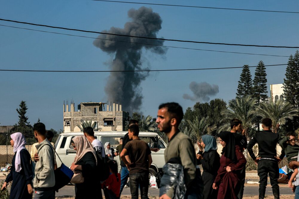 Smoke from Israeli bombardment rises behind people fleeing south from Gaza City and other parts of the northern Gaza Strip, as they walk along a highway on Nov. 9. (AFP via Getty Images)