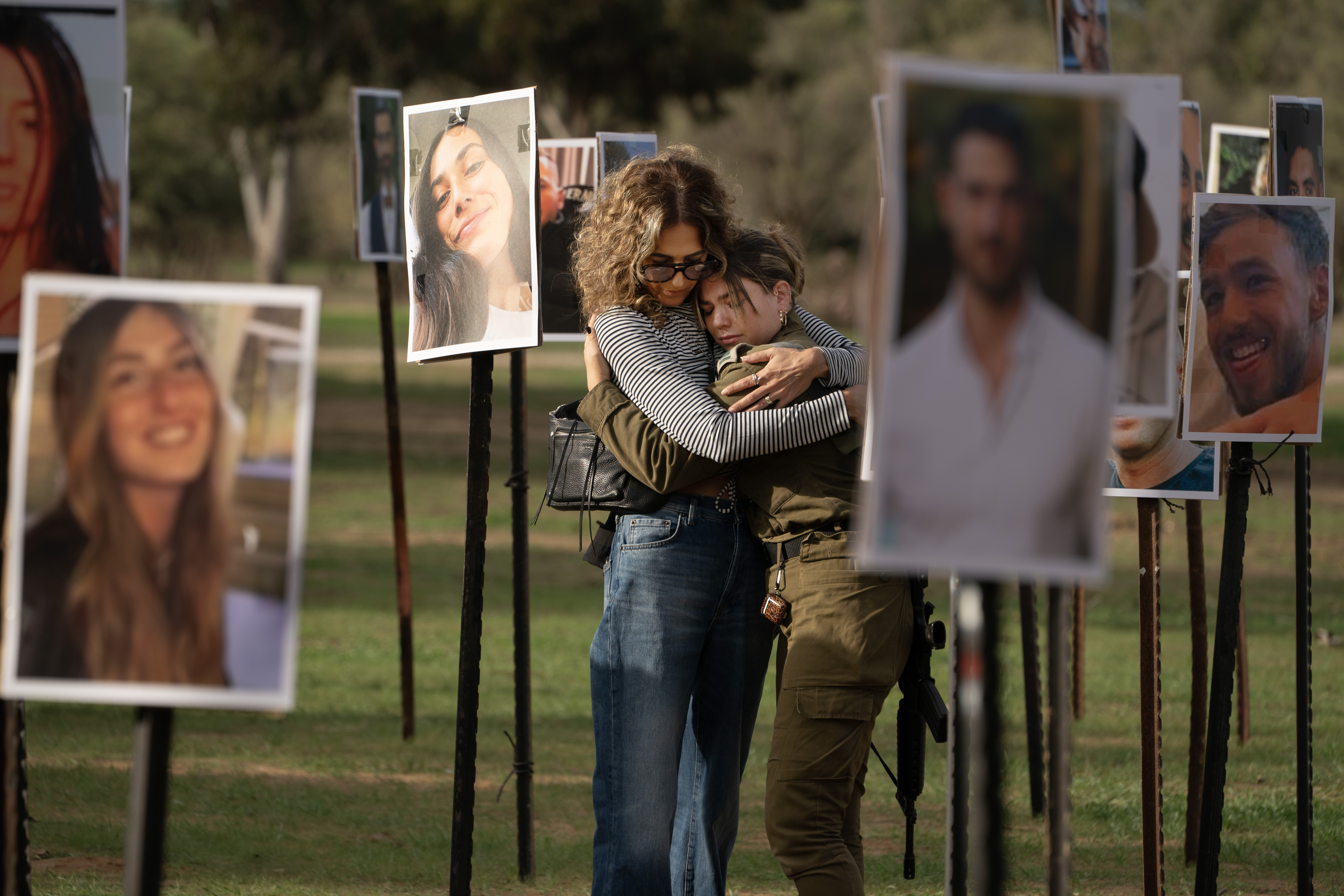 Sigal Manzuri, whose daughters Norelle and Roya were killed in the Hamas-led attack on the Nova music festival on Oct. 7, embraces one of their friends. Surrounding them are photos of people killed and taken hostage by Hamas militants, displayed at the site as DJs spin music to commemorate victims, near Kibbutz Re'im, Tuesday. (Maya Levin for NPR)