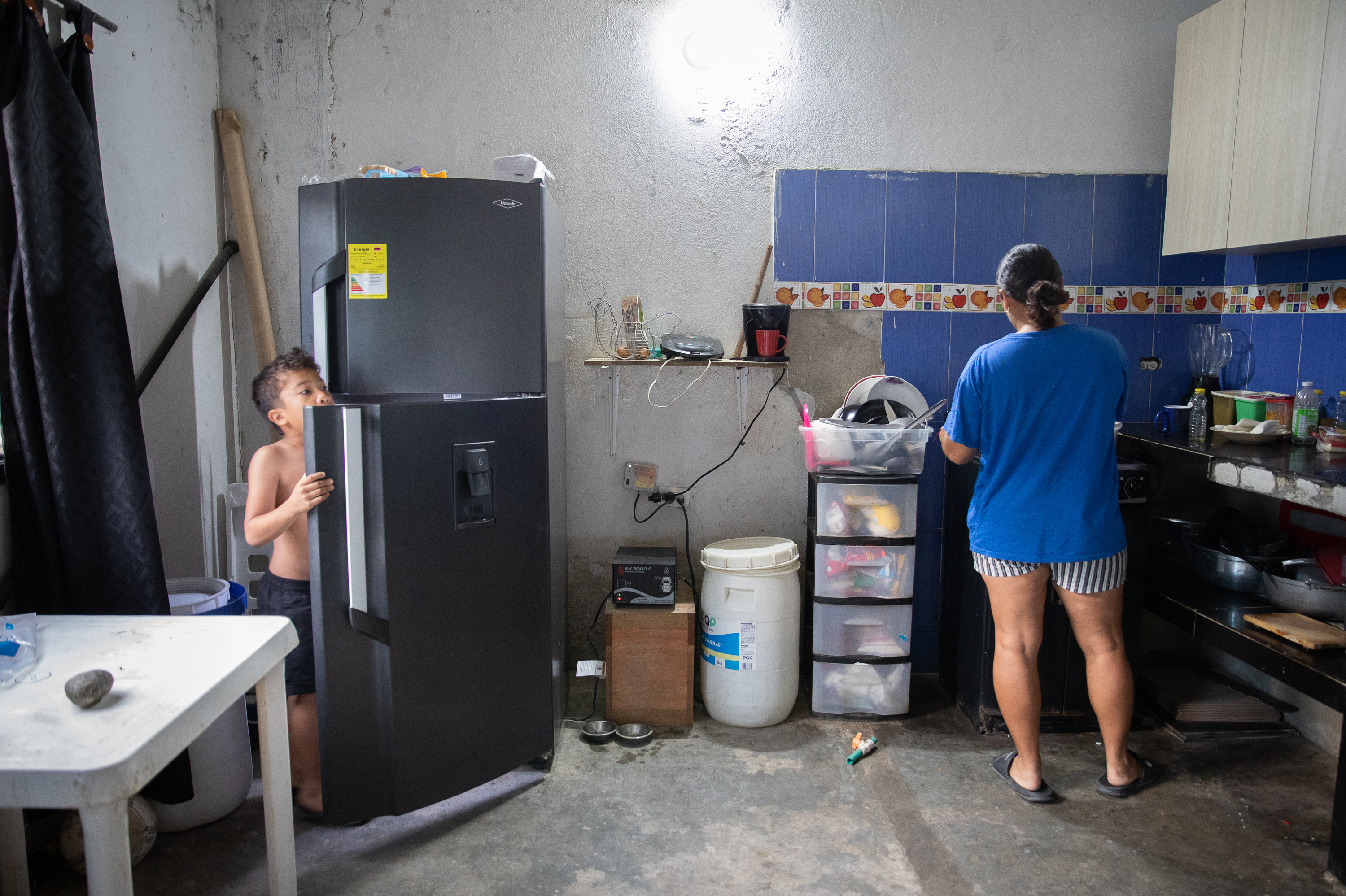 July prepares breakfast for her 6-year-old son, Samuel. She and her husband spend a significant amount of their monthly income to purchase water for drinking. The white container by her side holds water for washing dishes.