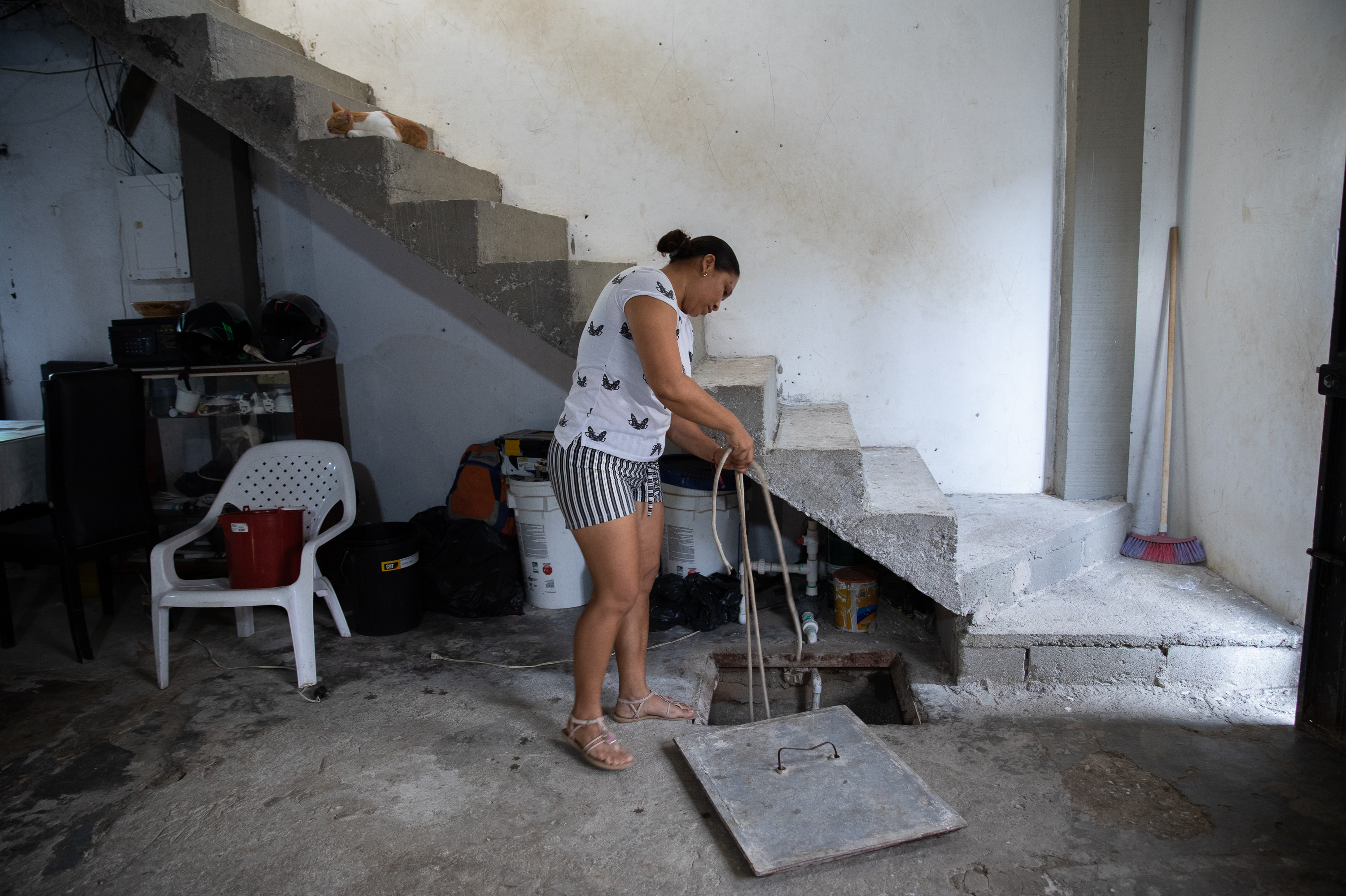July Merino shows how she retrieves water from the alberca in her home. The concrete cistern can store about two weeks of water that her family uses to do laundry, wash dishes and flush the toilet.