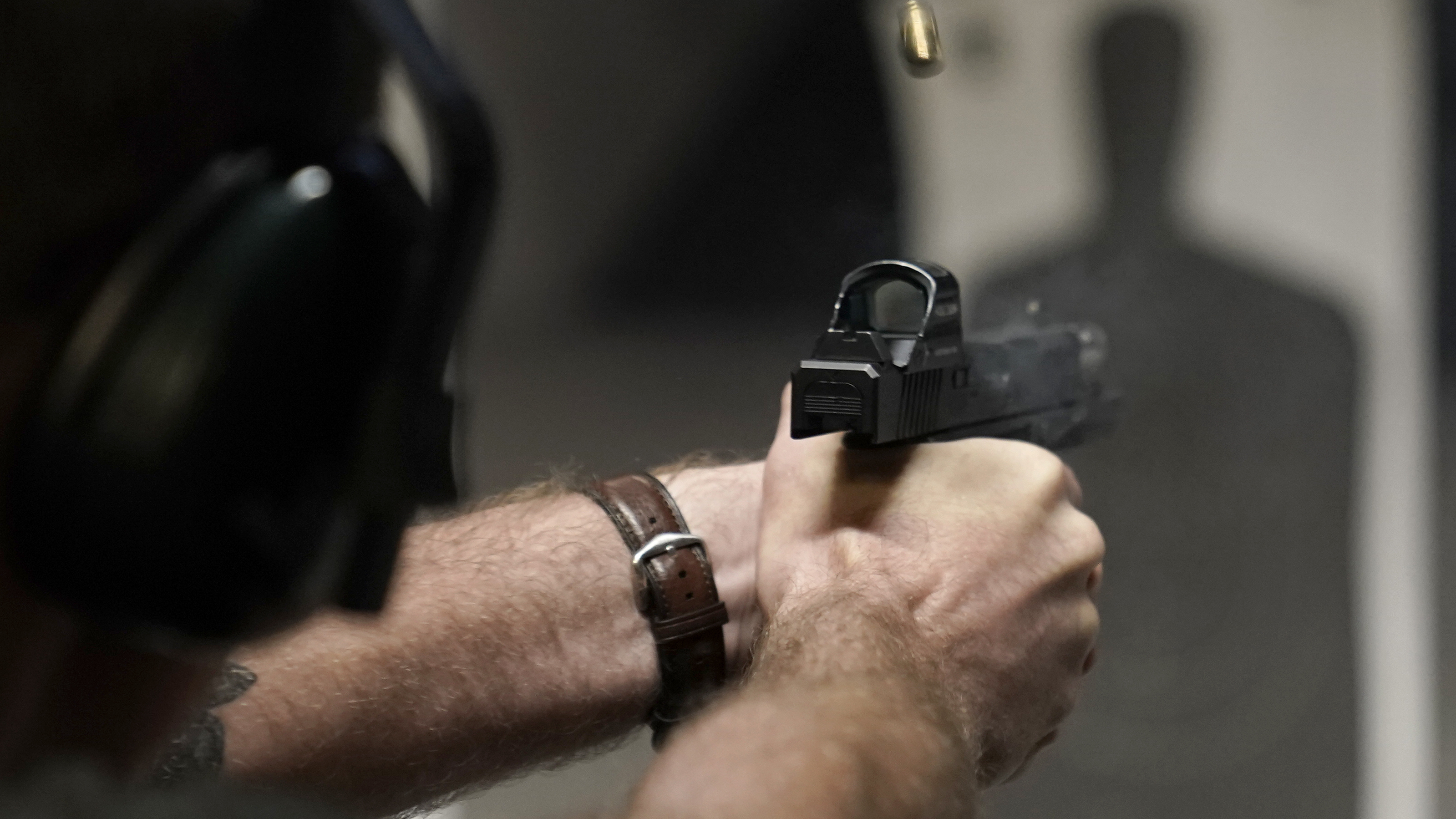 A man fires his pistol at an indoor shooting range during a qualification course to renew his Carry Concealed handgun permit at the Placer Sporting Club, July 1, 2022, in Roseville, Calif.