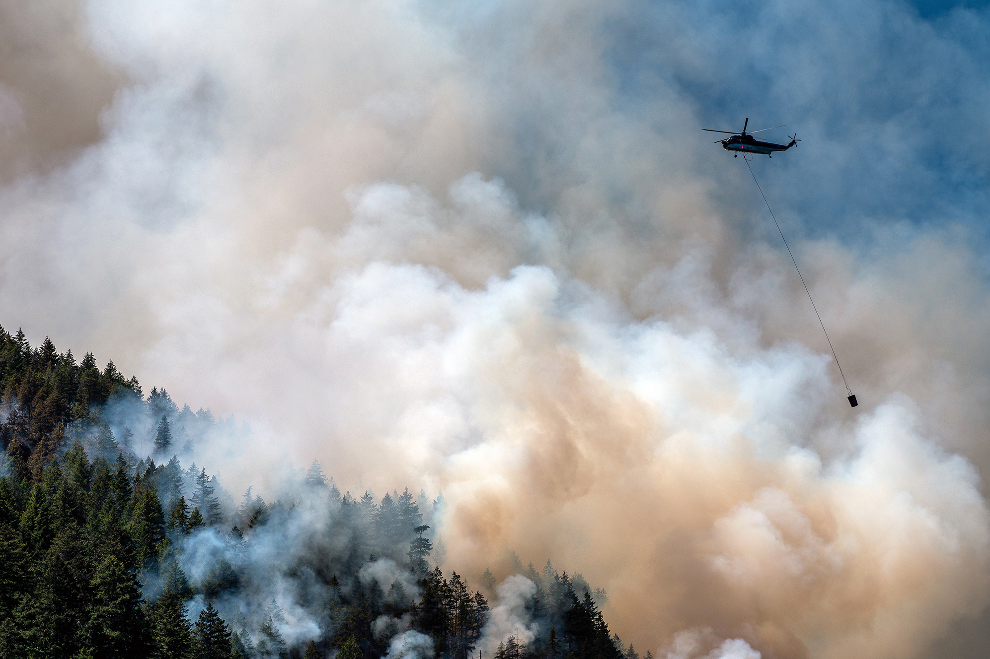 A helicopter flies above a wildfire burning in Canada this summer. Smoke from these wildfires floated hundreds of miles, blanketing much of North America in toxic air. (Bloomberg via Getty Images)