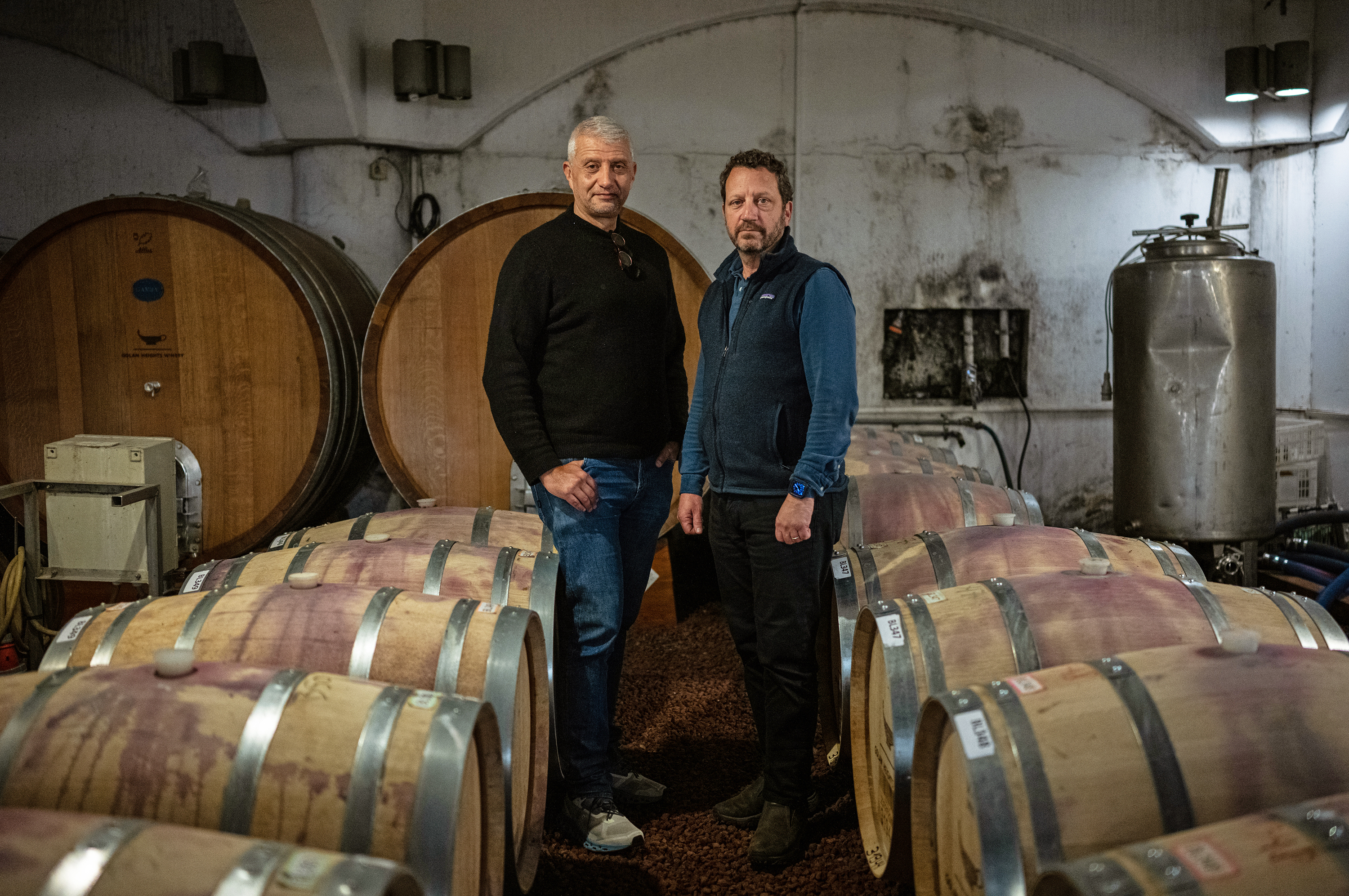 Golan Heights Winery CEO Assaf Ben Dov (left) and head winemaker Victor Schoenfeld are photographed in one of the winery's cellars in Katzrin, the Golan Heights, on Jan. 8, 2024. (Tamir Kalifa for NPR)