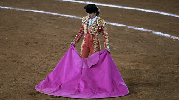 A female bullfighter stands in an arena holding a pink cape.