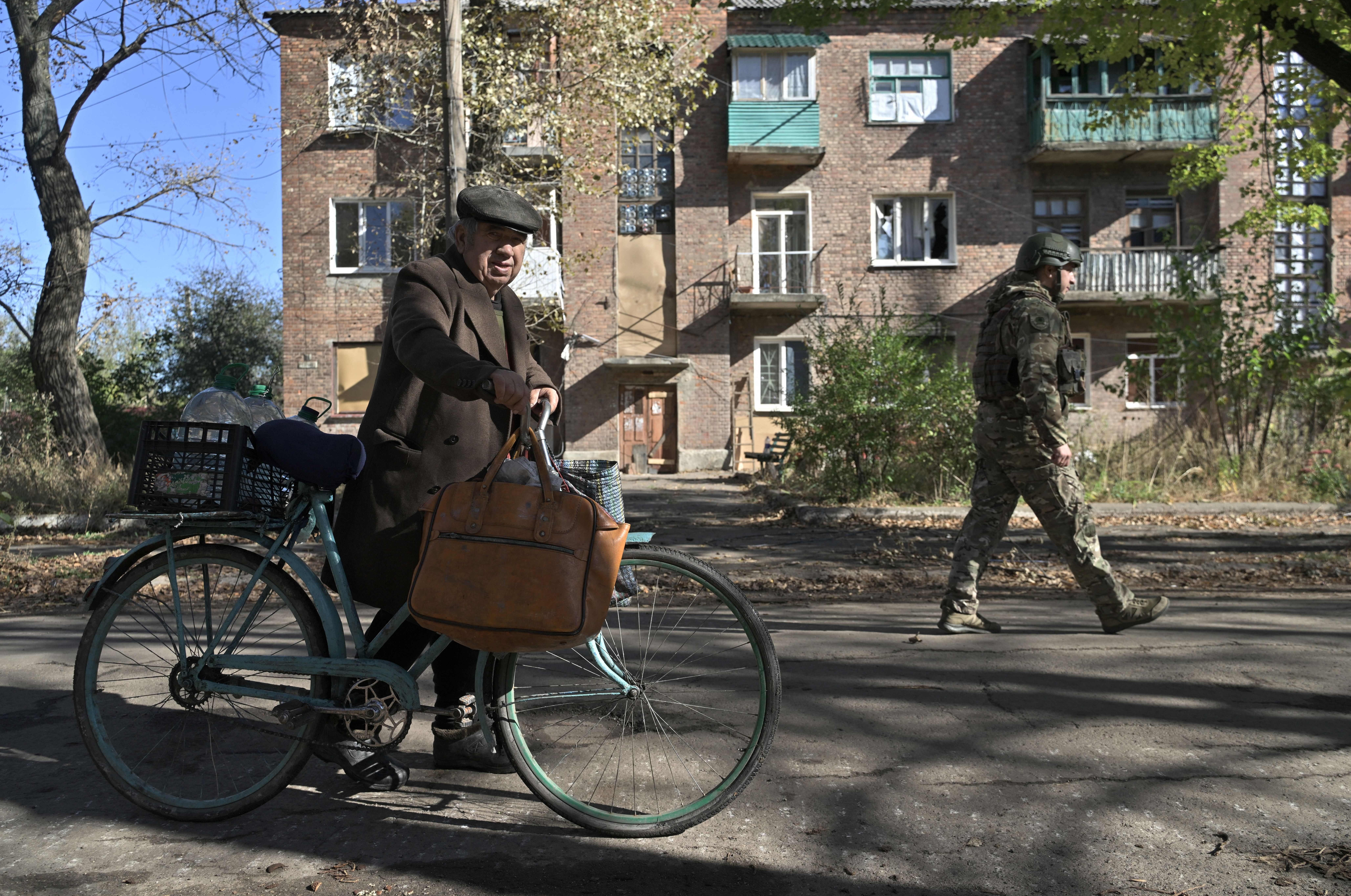 A Ukrainian policeman (R) walks next to 84-year-old resident Mykola (L) pushing his bicycle on a street in the frontline town of Chasiv Yar, in the Donetsk region on October 11, 2023, amid the Russian invasion of Ukraine. Explosions are near-constant in the small town, whose buildings are scored with holes from shelling. (AFP via Getty Images)