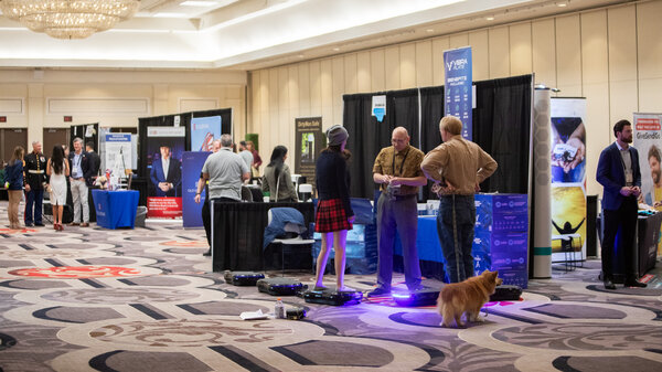 People mill about a convention center with stalls and booths.