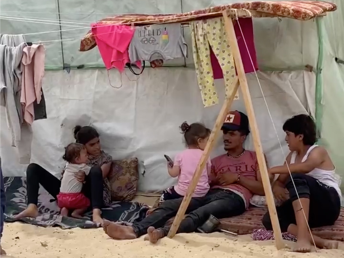 Displaced Palestinians in Rafah sit in the shade of their tent on a 100-degree day in the Gaza Strip. (Anas Baba for NPR)