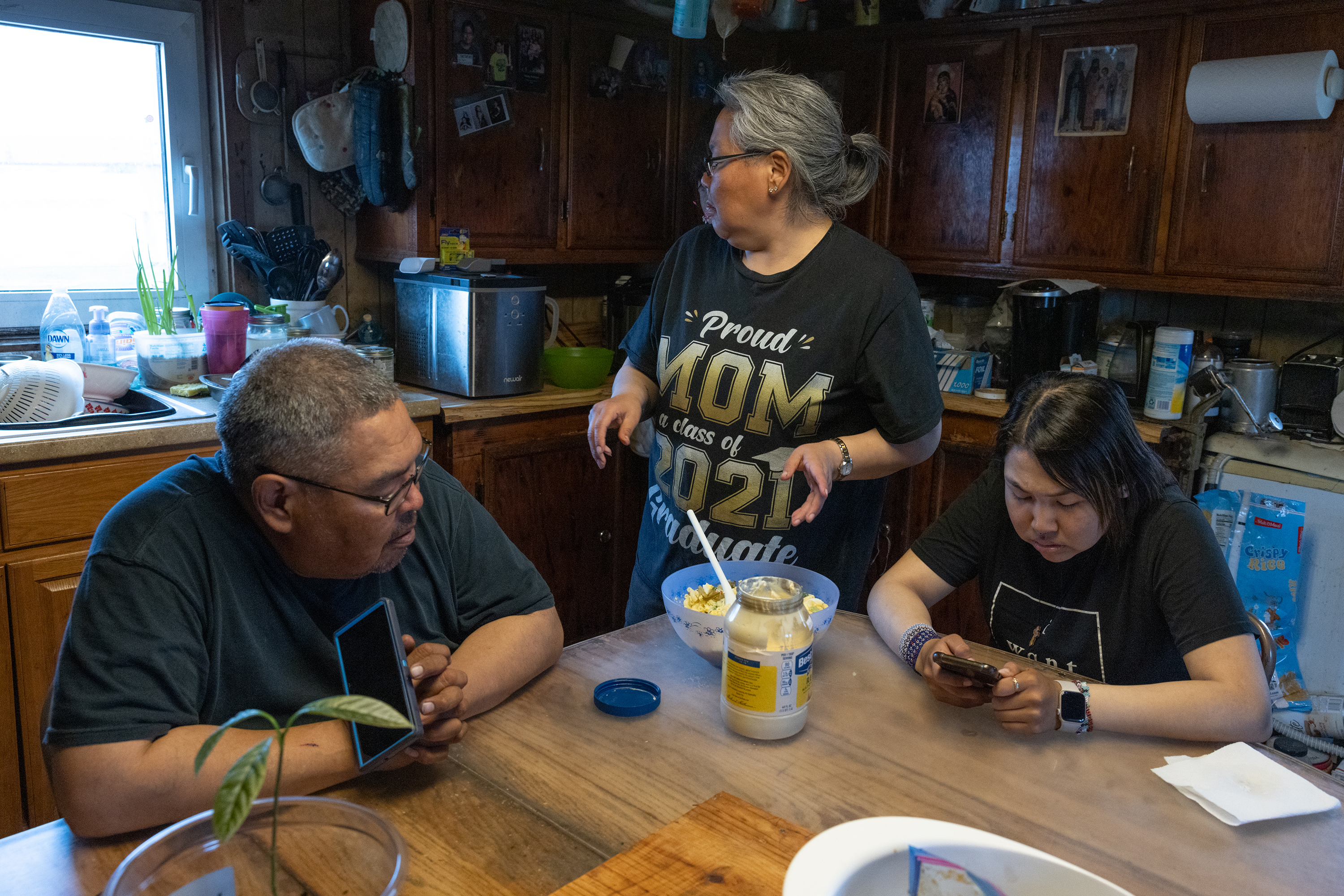 Wilson, Bertha and their daughter Angela in the kitchen at their home in Kasigluk, Alaska. This year, for the first time, Wilson and Bertha said they can sometimes hear water hitting the outside corner of the house. Erosion, permafrost thaw and flooding have eaten away at the land and caused the foundation of the home to sink.