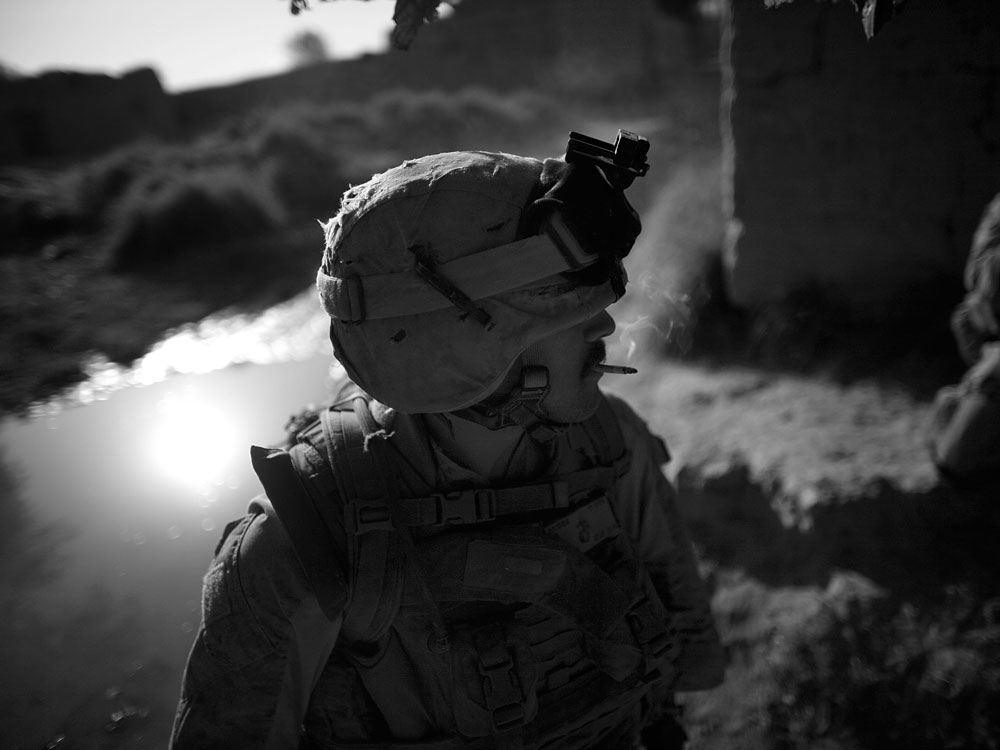 Lance Col. Eric Jenkins blows out the final draft of a cigarette while taking a break from early morning patrol in Helmand River valley. (NPR)