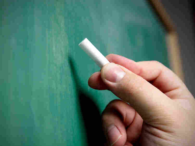A hand poised to write on a chalkboard.