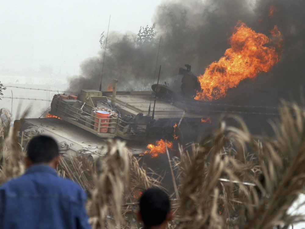Iraqis look at a burning U.S. Army Abrams battle tank on March 10, 2006, after an IED exploded on a highway in eastern Baghdad. (Getty Images)