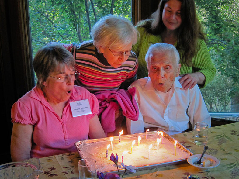 Camp director Caitlin Morgan (upper right) says people with dementia often don't get the interaction they need. "Just because someone gets a diagnosis of Alzheimer's or other dementia doesn't mean life is over," Morgan says. Campers (from left) Deborah Gallagher, Jeanne Vasconcelles and Jimmy Johnson celebrate their birthdays together after Saturday night's dinner. (Cindy Carpien/NPR)