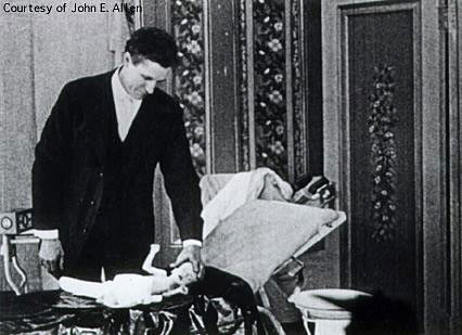 Dr. Haiselden manually inspects the head of a new born baby which is lying on an examination table.