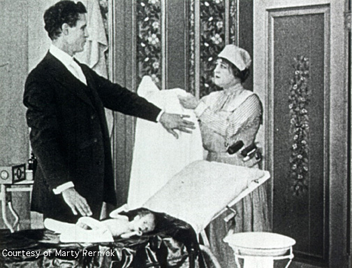 As a nurse tries to hand him his operating gown, Dr. Haiselden,  who is standing over a newborn baby, waves the gown off with his arm..