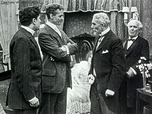 Dr.  Haiselden, arms crossed, stands confidently facing two older doctors in front of a female patient's bed in her home.