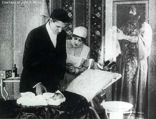 Dr. Haiselden and his nurse look over the newborn child who he has let die.  In the back ground, a translucent Jesus stands with the baby in his arms.