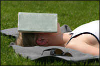 Woman asleep outside, shielding her face from sun with a book.
