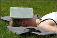 Woman asleep outside, shielding her face from sun with a book.